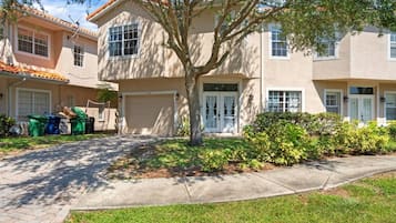 A two-story residential building with a garage, a tree in the front yard, and a well-maintained lawn.
