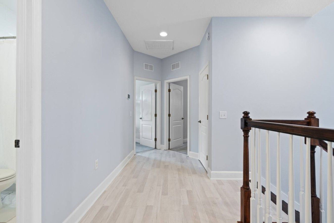 A hallway with light-colored walls and wooden flooring, leading to a door at the end.