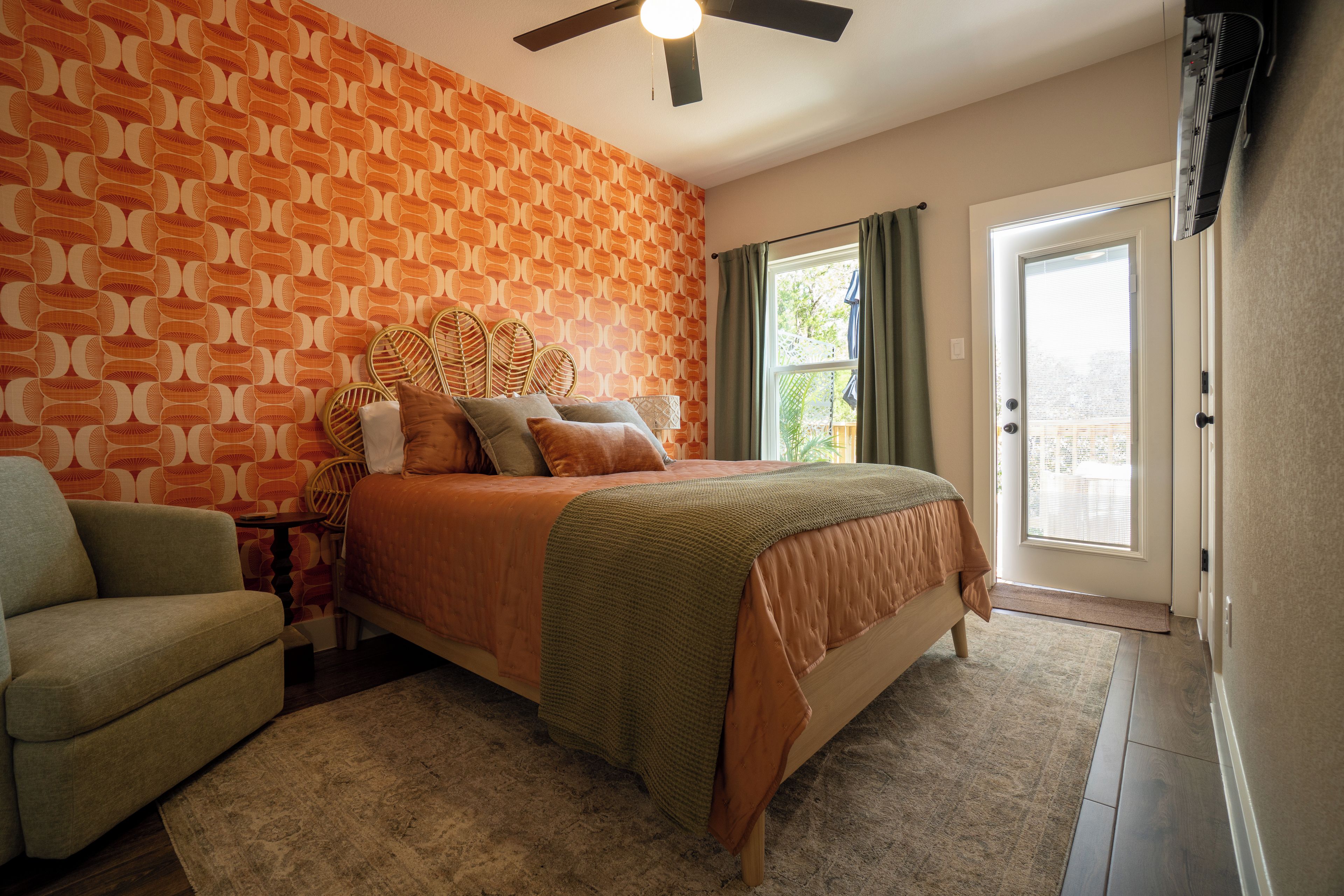A bedroom with a patterned wall, a bed with multiple pillows, a chair, and a door leading to a balcony.