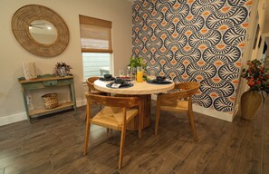 Un coin repas comprenant une table ronde, deux chaises, un miroir décoratif et un mur orné d’un motif.