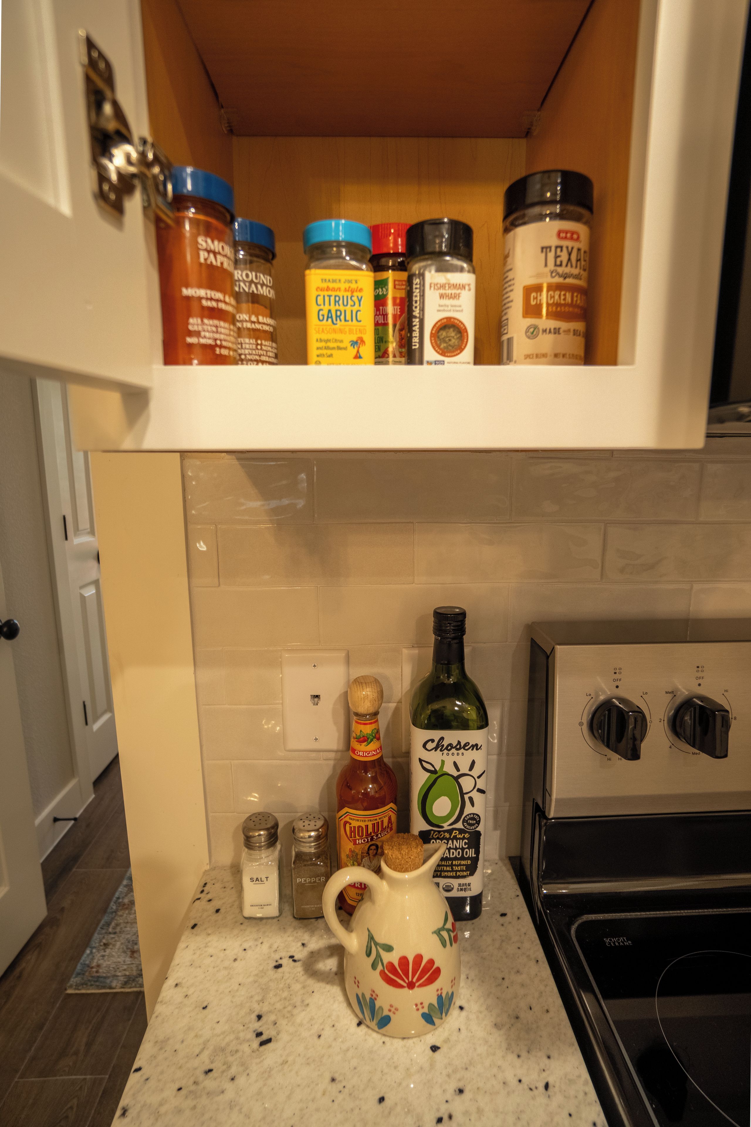 A kitchen with a spice rack, salt and pepper shakers, a bottle of hot sauce, and a coffee maker.