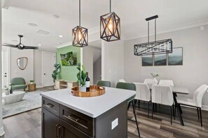 A modern kitchen with a central island, pendant lighting, and a dining area with white chairs. - Downtown Tampa Retreat | Dining & Riverwalk (Tampa)