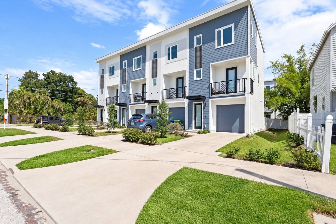 A multi-story residential building with a garage, a driveway, and a well-maintained lawn.