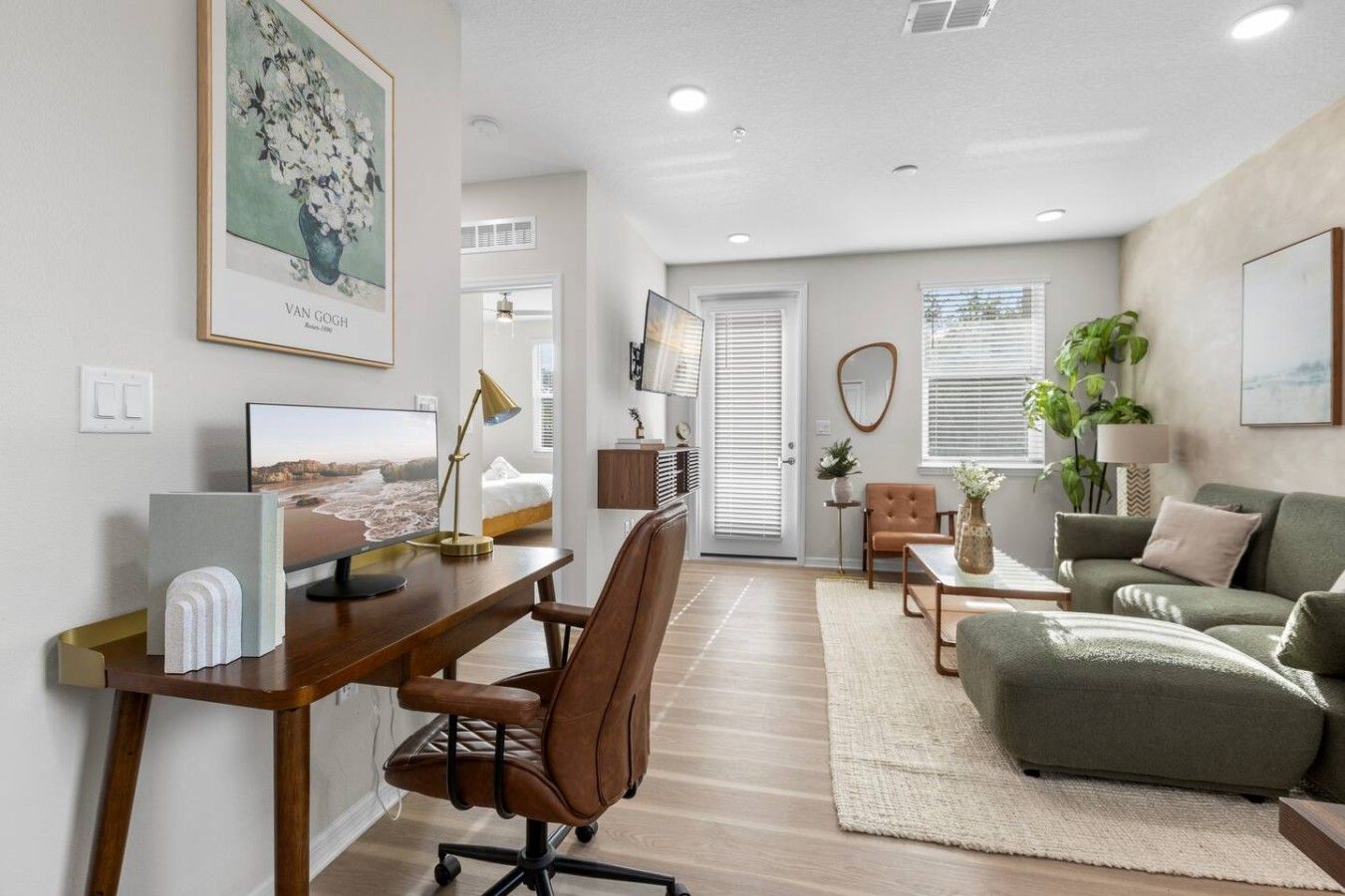 Un salon moderne avec un bureau, un fauteuil en cuir marron, un canapé vert et un téléviseur.