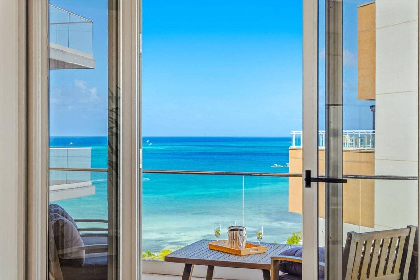 A balcony with a view of the ocean and a table with a tray of glasses.