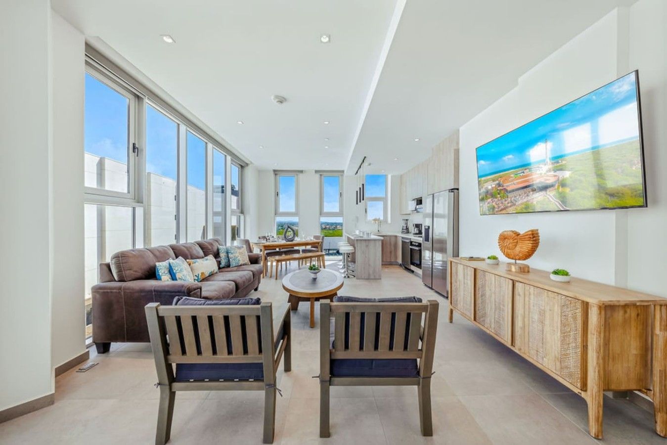 A spacious living area with a sofa, chairs, a dining table, and a kitchen with modern appliances.