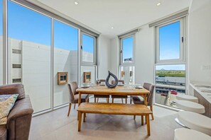 A modern dining area with a wooden table and chairs, large windows, and a view of the cityscape. - The Reef 7C - Island Horizon (Noord)
