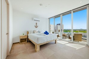Ein Schlafzimmer mit einem großen Bett, einem Nachttisch, einer Wand-Klimaanlage und Blick ins Freie durch eine Glastür.
