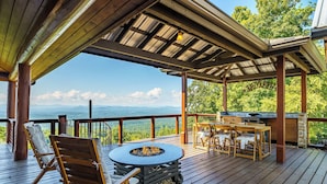 Una terraza exterior cubierta con una chimenea, asientos y una zona de barbacoa, con vistas a un paisaje montañoso.