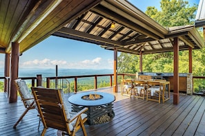 A covered outdoor deck with a fire pit, seating, and a grill area, overlooking a mountainous landscape. - Cloud Top Lodge - Escape to a Heavenly View (Murphy)
