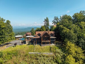 A lodge with a large wooden structure, a covered parking area, and a view of the surrounding forest and mountains. - Cloud Top Lodge - Escape to a Heavenly View (Murphy)