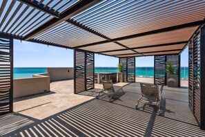 A covered outdoor seating area with a view of the ocean, featuring a pergola structure and a table with chairs. - The Reef 2C - Coral Sky (Noord)