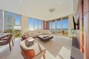 A spacious living room with a large sofa, a dining area with a table and chairs, and large windows offering a view of the ocean. - The Reef 4A - Blue Horizon (Noord)
