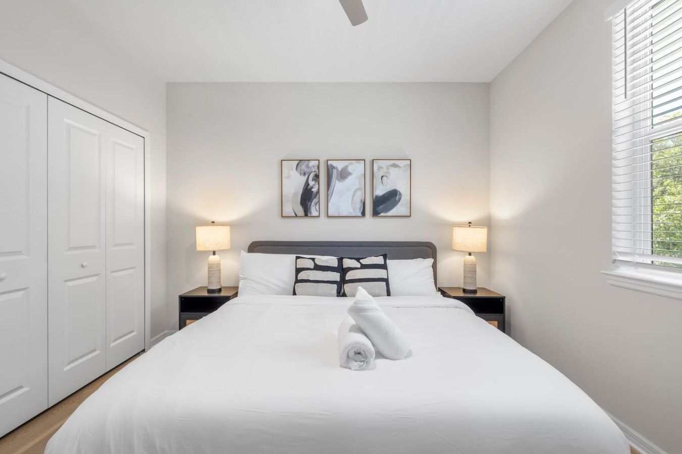 A bedroom with a bed, two bedside lamps, a ceiling fan, and a window with blinds.