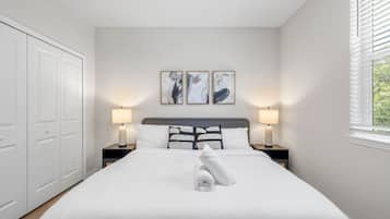 A bedroom with a bed, two bedside lamps, a ceiling fan, and a window with blinds.