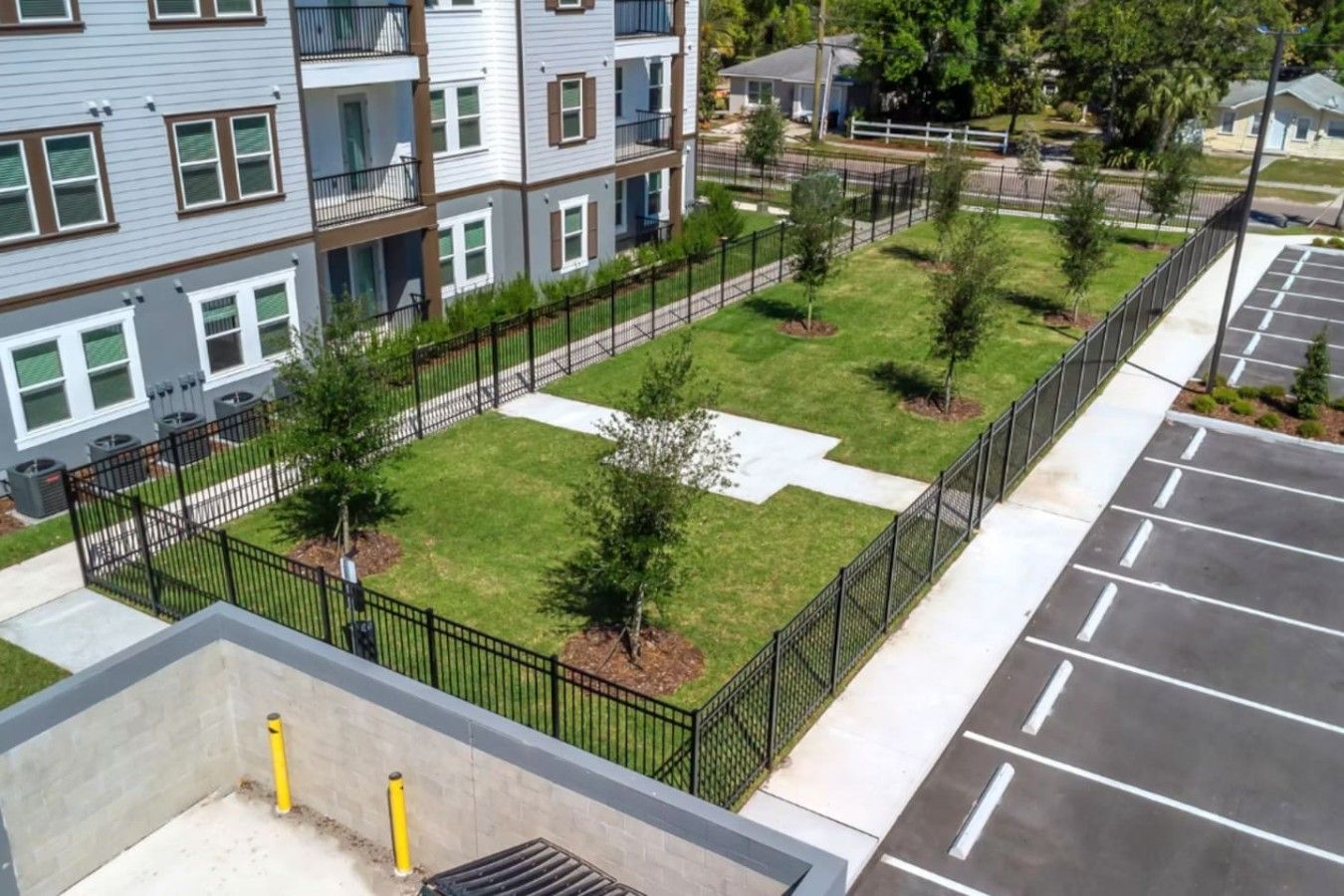 A multi-story residential building with a fenced courtyard, a parking area, and a visible cross-shaped pavement.
