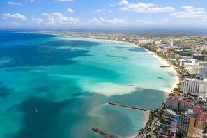 An aerial view of a coastal city with a beach, buildings, and a clear sky. - The Reef 6A - Ocean Pearl (Noord)