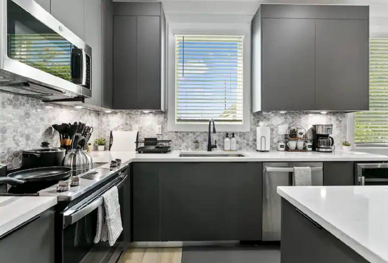 A modern kitchen with dark cabinetry, a microwave, stove, and a window with blinds.