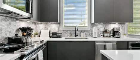 A modern kitchen with dark cabinetry, a microwave, stove, and a window with blinds.