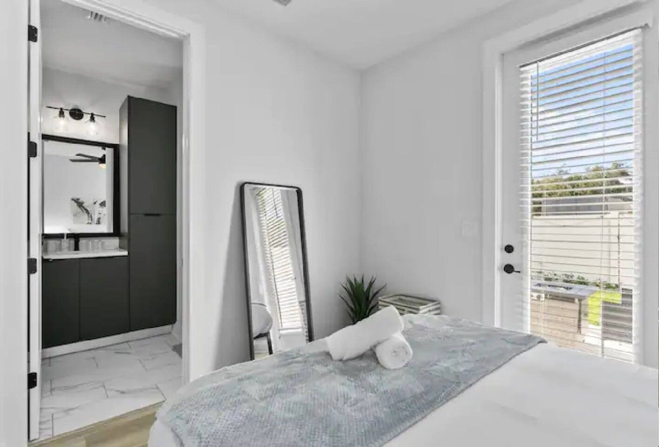 Un dormitorio moderno con una cama, un espejo grande, una planta en maceta y vistas al exterior a través de una ventana.