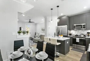 A modern kitchen with a central island, built-in appliances, and a dining area with a glass table and chairs. - Modern Downtown Tampa Townhome | Near Riverwalk (Tampa)