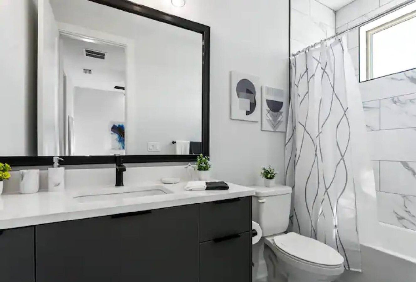 Ein modernes Badezimmer mit einem weißen Waschbecken, dunklen Schränken, einer Toilette und einem Duschvorhang mit Wellenmuster.