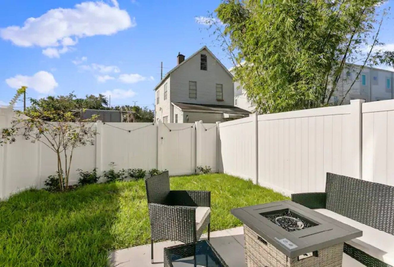 A backyard with a fire pit, two chairs, and a white fence.