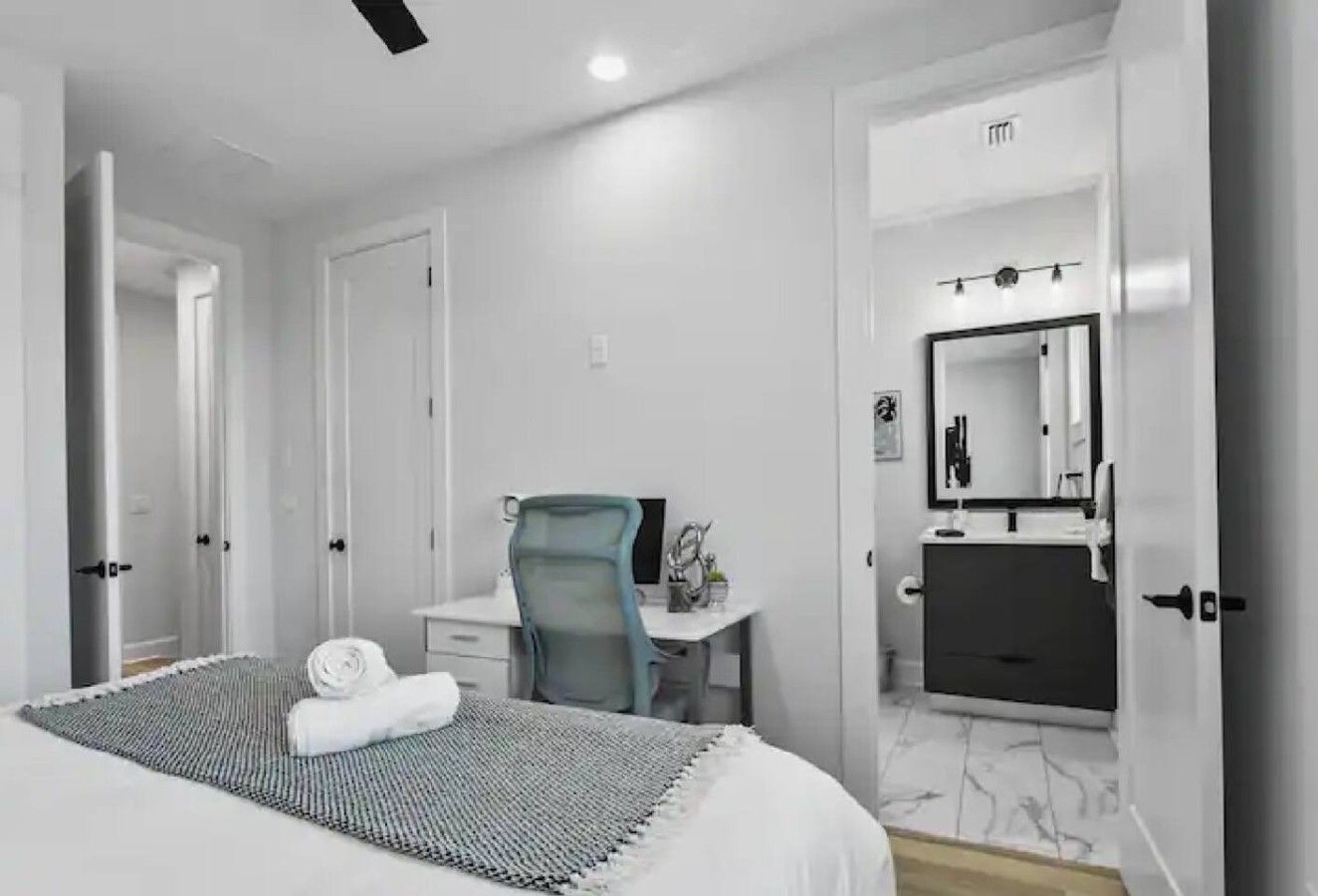 Quarto de hotel com cama, escrivaninha, cadeira e banheiro com espelho.
