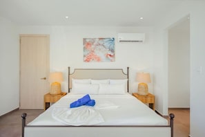 A neatly made bed with white linens and a blue towel, flanked by two bedside lamps on wooden nightstands. - The Reef 5C - Ocean Haven (Noord)