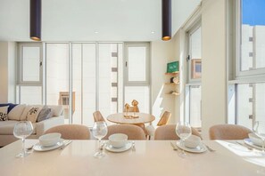 A dining area with a round table, white chairs, and a sofa in the background. - The Reef 5C - Ocean Haven (Noord)