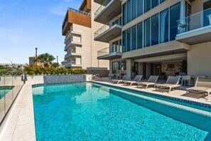 Um hotel moderno com piscina, espreguiçadeiras e vista para os edifícios ao redor.