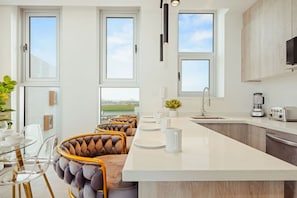 Eine moderne Küche mit einer großen Kochinsel, Barhocker und Blick ins Freie.