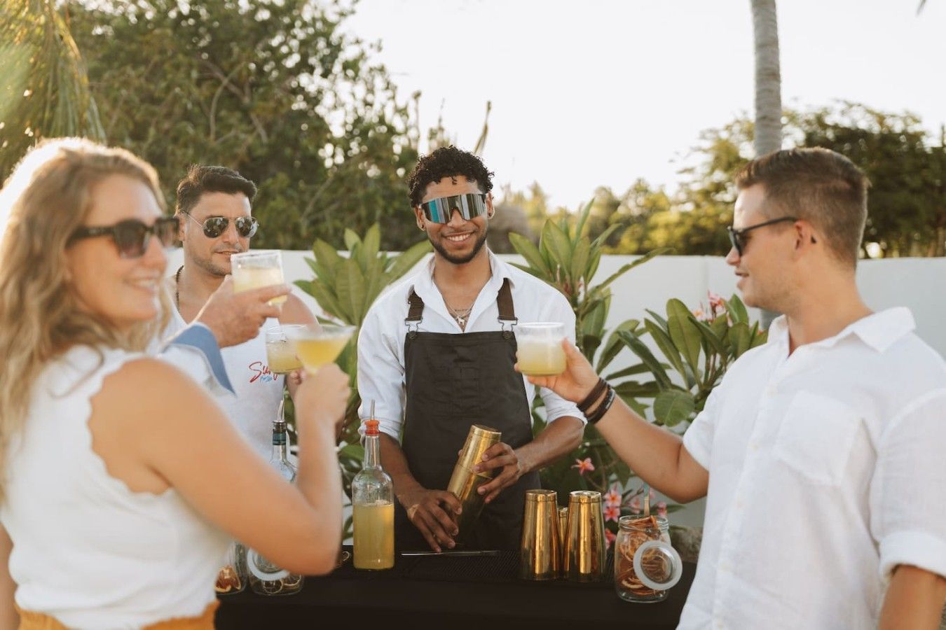 Eine Gruppe von Menschen an einer Bar im Freien mit Getränken und einem Barkeeper.