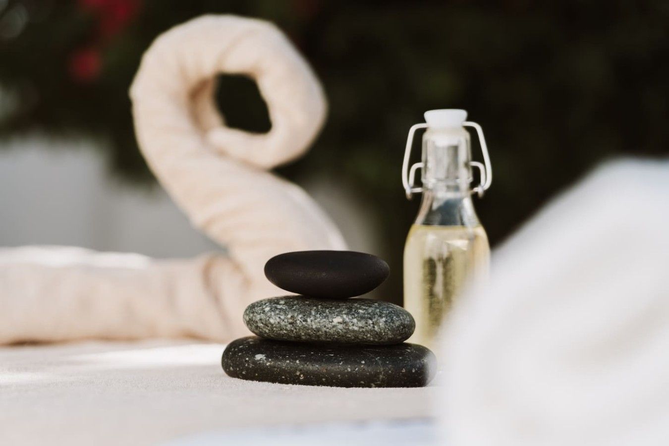 Ein Stapel glatter Steine und eine Flasche Flüssigkeit, möglicherweise ein Wellnessprodukt, auf einer weißen Oberfläche.