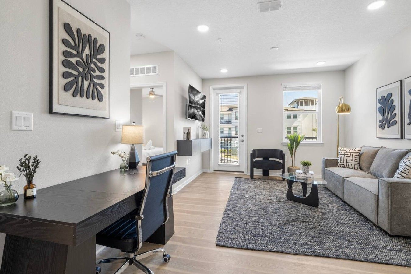 A modern living room with a dark wood desk, a grey sofa, and a black armchair.