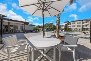 An outdoor patio with a round table and white chairs, a pool, and a building with balconies. - Cozy Largo Stay | Pool, Gym & Free Parking (Largo)