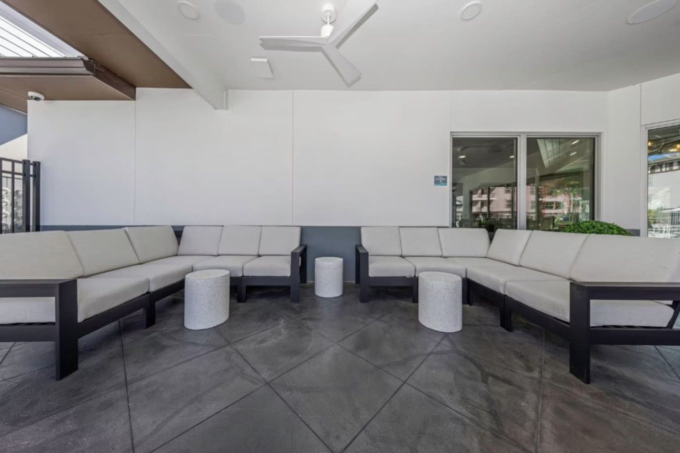 A modern lounge area with a sectional sofa, two round stools, and a ceiling fan.