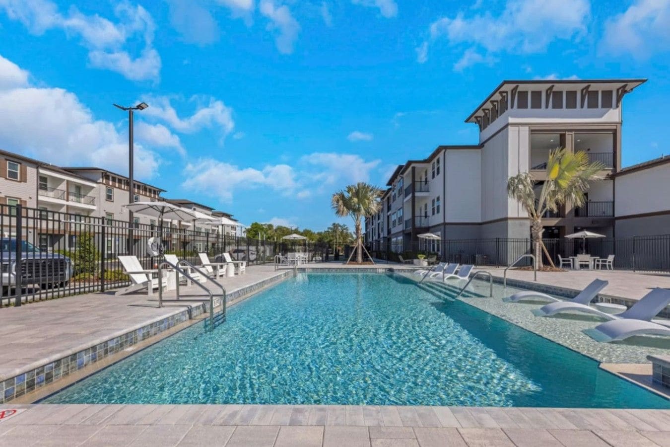 A swimming pool with lounge chairs and a palm tree, surrounded by multi-story buildings.