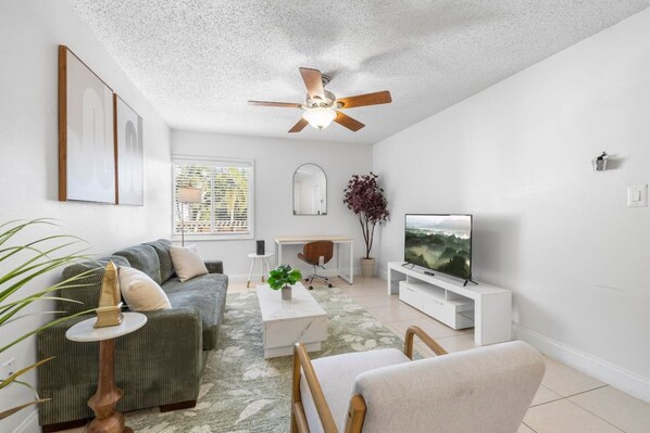 A modern living room with a sofa, coffee table, TV, and ceiling fan. - Bayside Tampa Escape | Pool, Gym & Parking (Tampa)