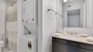 A modern bathroom with a built-in washer and dryer, a large mirror, and a vanity with a sink and towel. - Bayside Tampa Escape | Pool, Gym & Parking (Tampa)