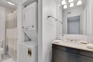 A modern bathroom with a built-in washer and dryer, a large mirror, and a vanity with a sink and towel. - Bayside Tampa Escape | Pool, Gym & Parking (Tampa)