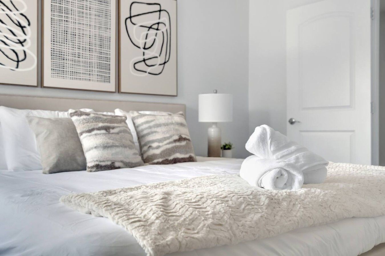 Ein Hotelzimmer mit einem ordentlich bezogenen Bett, einer weißen Tür und abstrakter Kunst an der Wand.