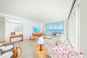 A modern living room with a large TV, a sofa, and a dining area with a table set for two. - The Reef 7B - Caribbean Vista (Noord)