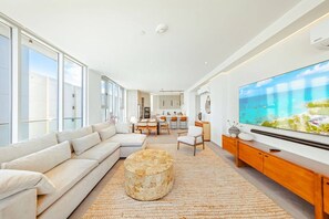 A modern living room with a large flat-screen TV, a sofa, a coffee table, and a dining area in the background. - The Reef 7B - Caribbean Vista (Noord)
