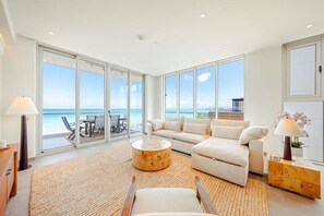 A spacious living room with a large sofa, a coffee table, and a view of the ocean through floor-to-ceiling windows. - The Reef 7B - Caribbean Vista (Noord)