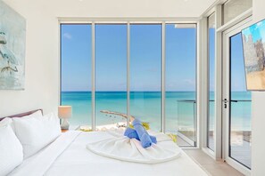 A hotel room with a large window offering a view of the sea and a balcony with a glass door. - The Reef 7B - Caribbean Vista (Noord)