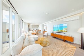 Een moderne woonkamer met een grote flatscreen televisie, een bank en een eethoek op de achtergrond.