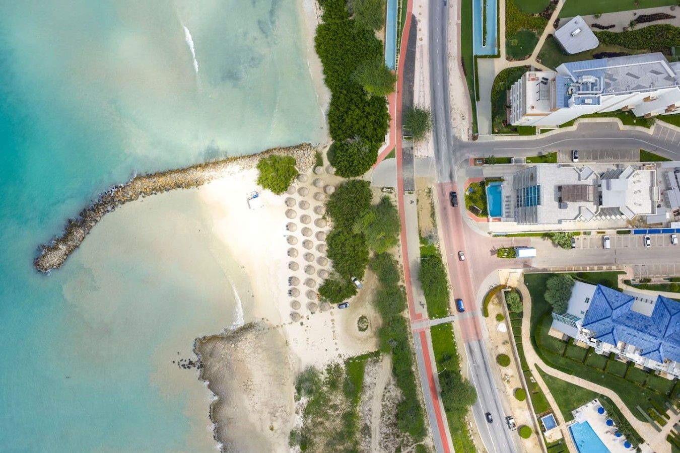 An aerial view of a coastal area with a beach, a road, and buildings.
