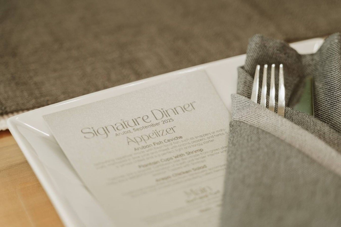 Ein festliches Menü mit dem Titel 'Signature Dinner', das Datum und den Ort zeigt, liegt auf einem Tisch mit gefaltetem Servietttuch und einer Gabel.