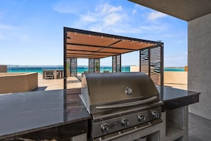Eine Außenküche mit Grill, einer Sitzecke und Blick auf den Ozean.